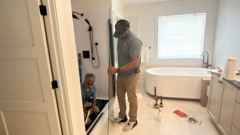 Two Bath Fitter installers working on a shower installation in a bright bathroom with a freestanding tub