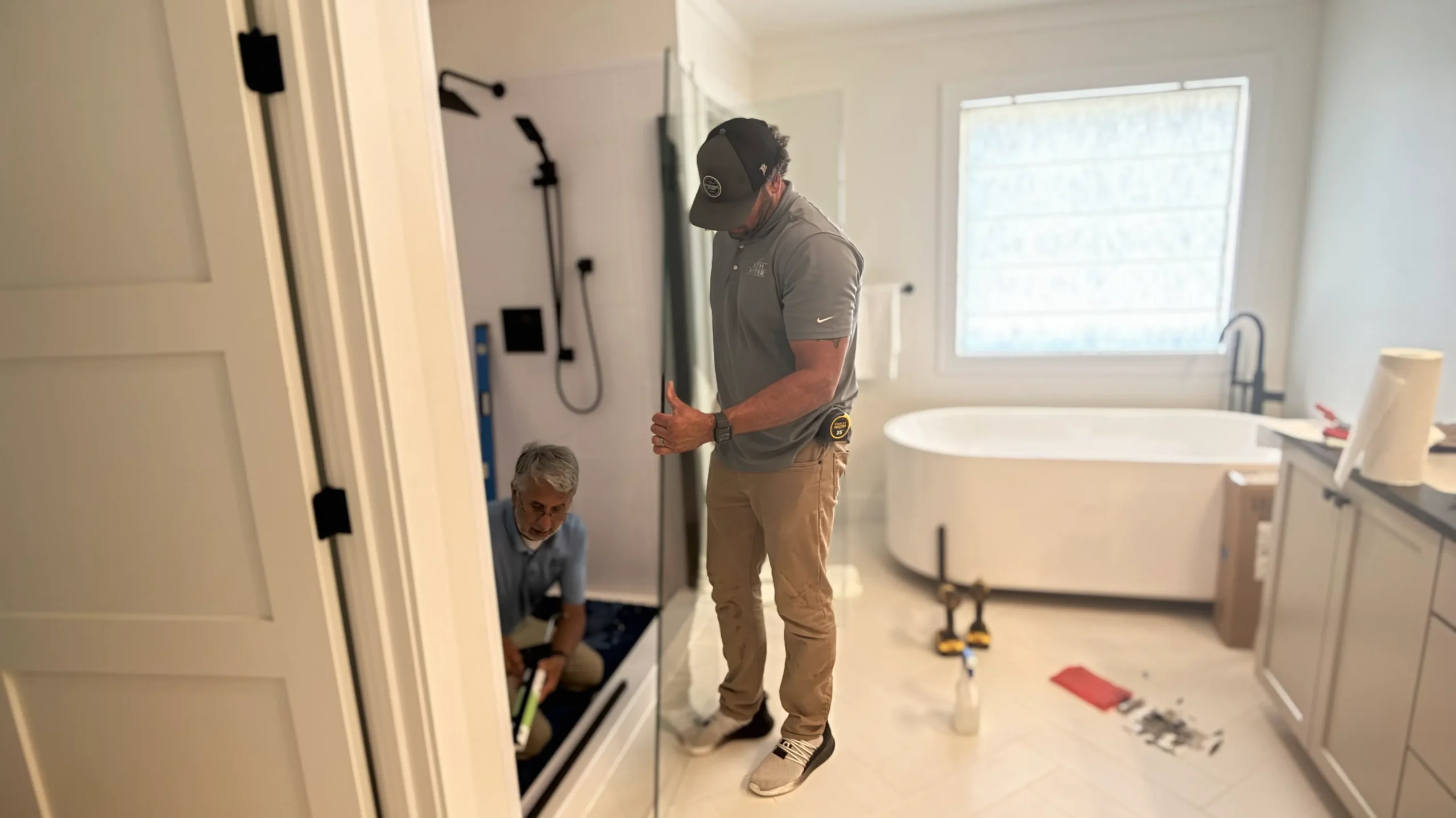 Two Bath Fitter installers working on a shower installation in a bright bathroom with a freestanding tub